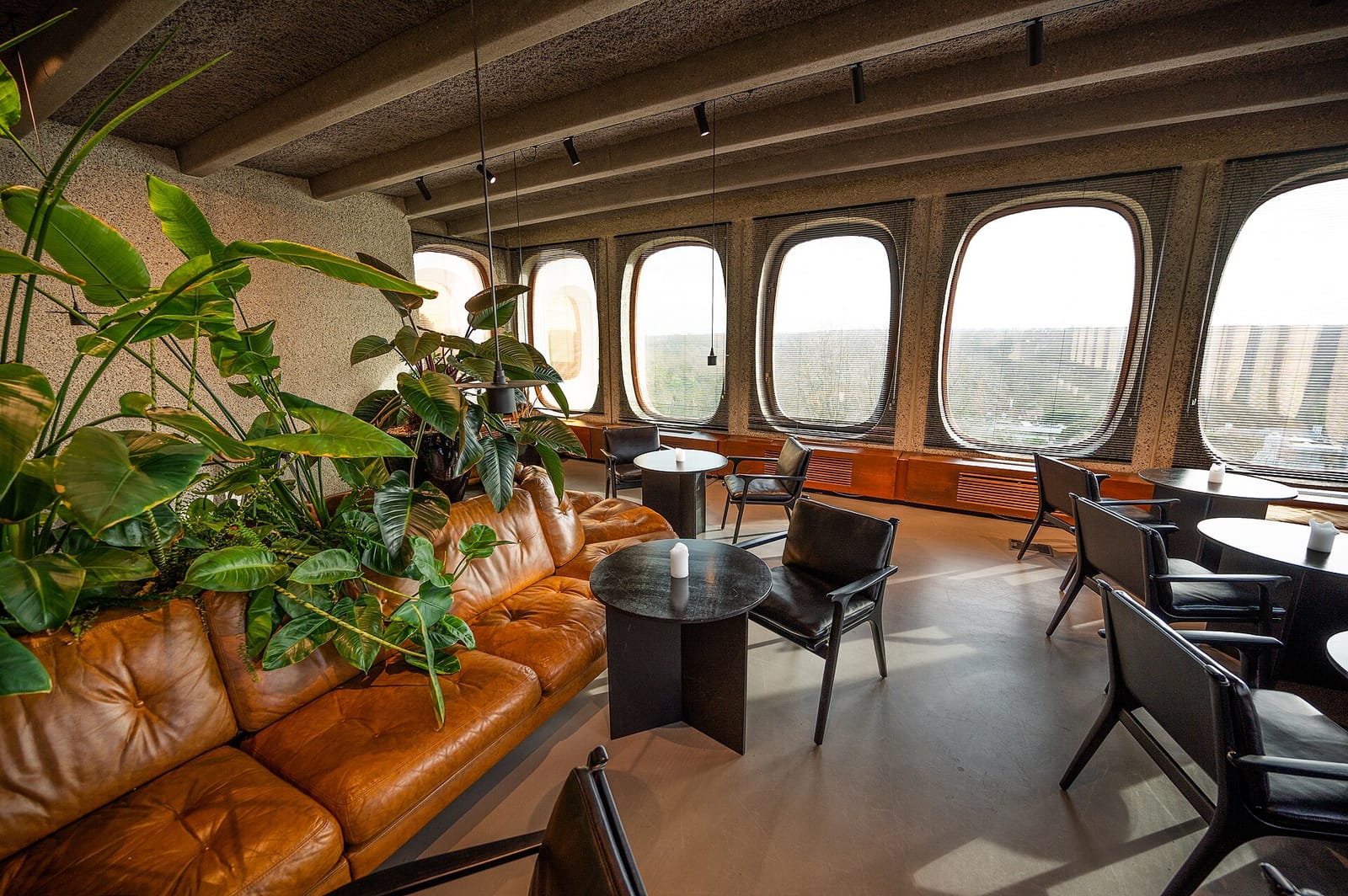A modern office lounge with leather sofas, plants and round windows over the city